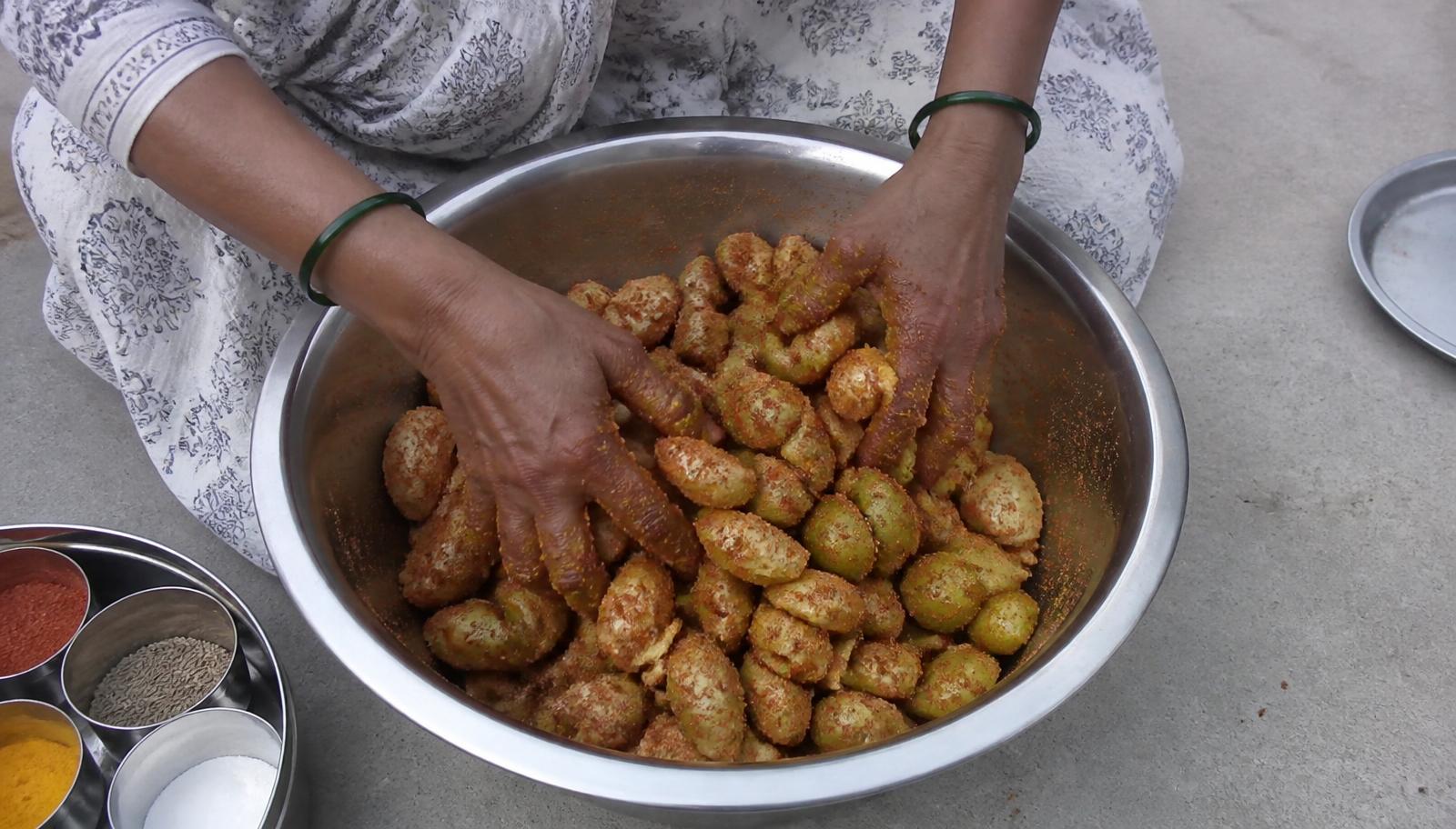 Glass jars of amla pickle being filled in a village kitchen